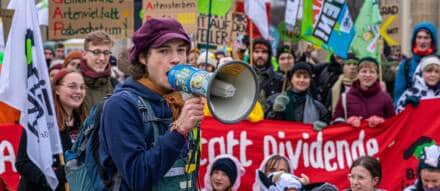 Menschen protestieren mit Schildern und Megafon in der Menge.