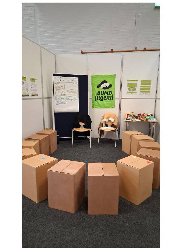 Workshopstand der BUNDjugend Berlin beim benbi mit Pinnwand und Papphockern in einem Halbkreis.