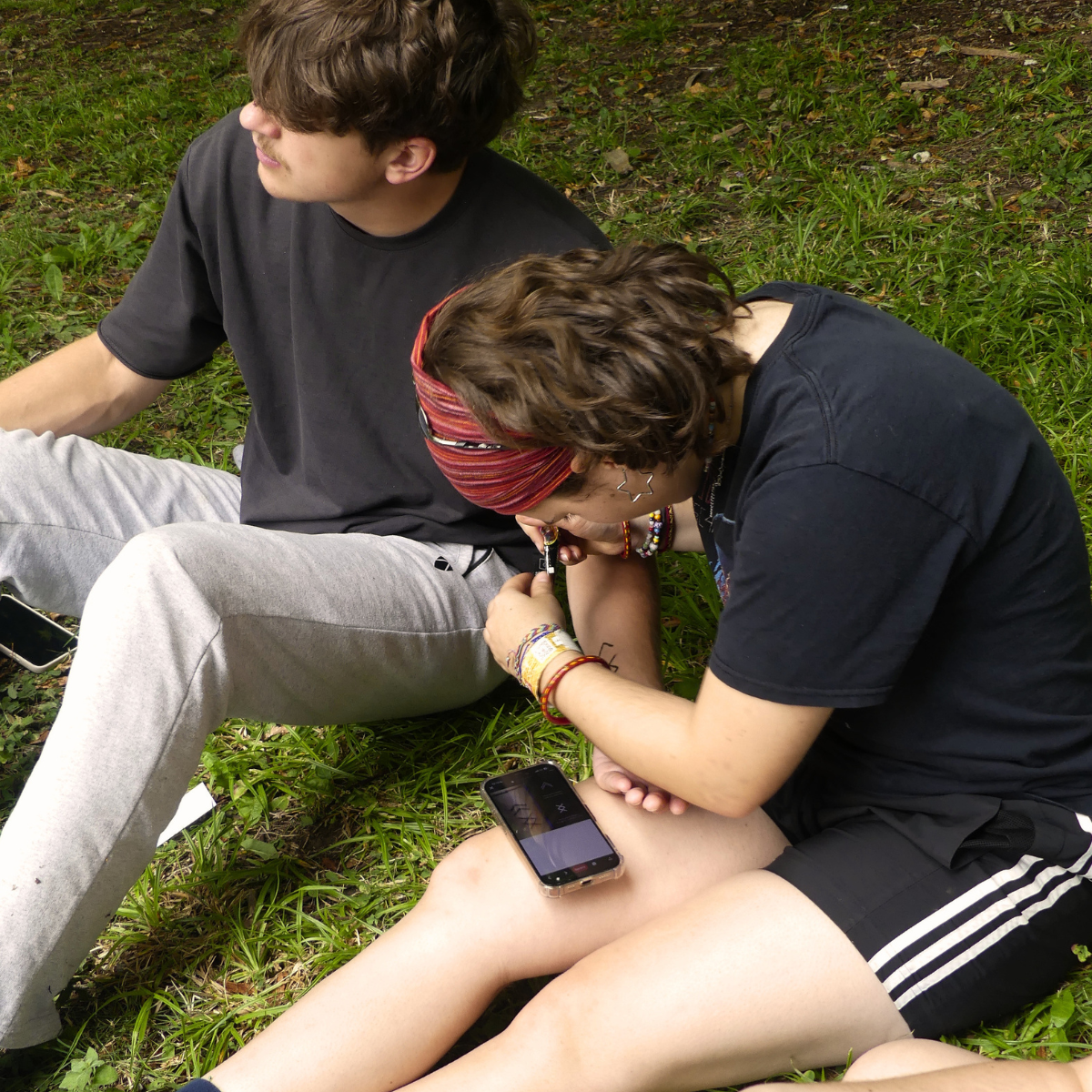 Zwei Personen sitzen im Gras und machen sich ein Henna-Tattoo