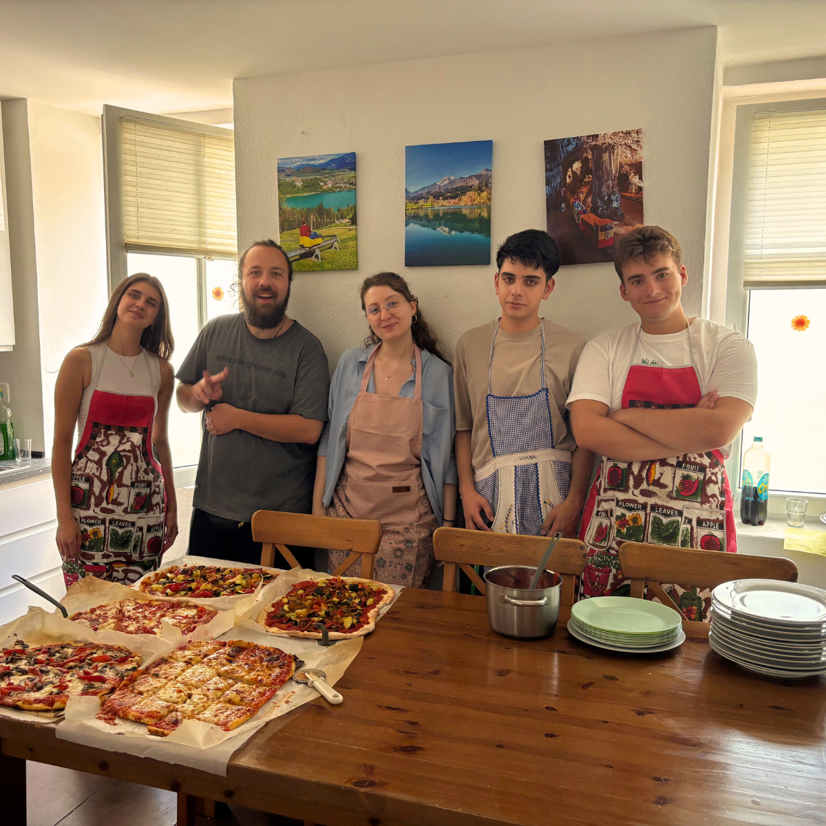 Fünf Personen mit Schürzen präsentieren selbstgemachte Pizzen