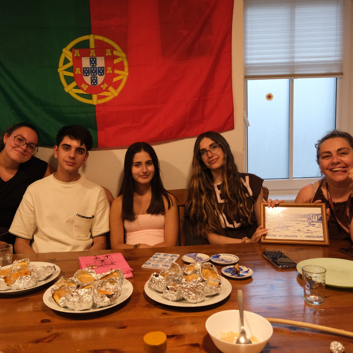 Fünf Personen präsentieren landestypische Gerichte vor portugiesischer Flagge