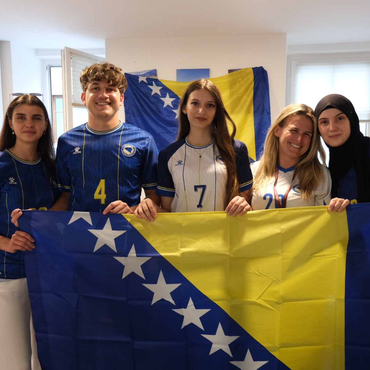 Fünf junge Menschen in Trikots halten eine Bosnien-Flagge